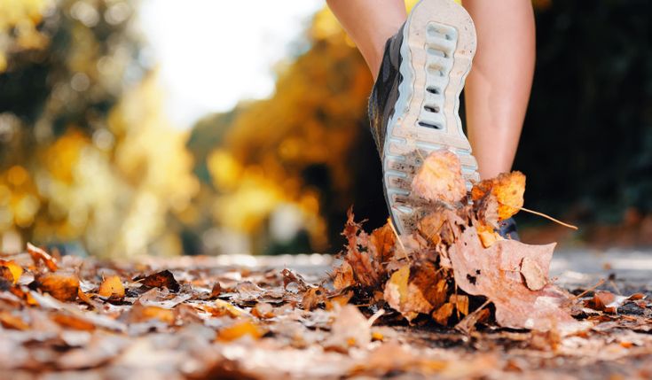 a woman's feet walking through leaves on the ground with her shoes in the air