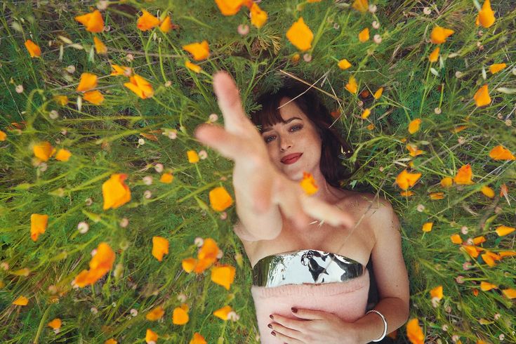 a woman laying in the grass with her hand up to her face and flowers all around her