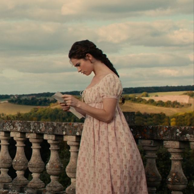 a woman in a pink dress is looking at her cell phone while standing on a balcony