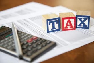 the word tax spelled out with blocks on top of paperwork and a calculator