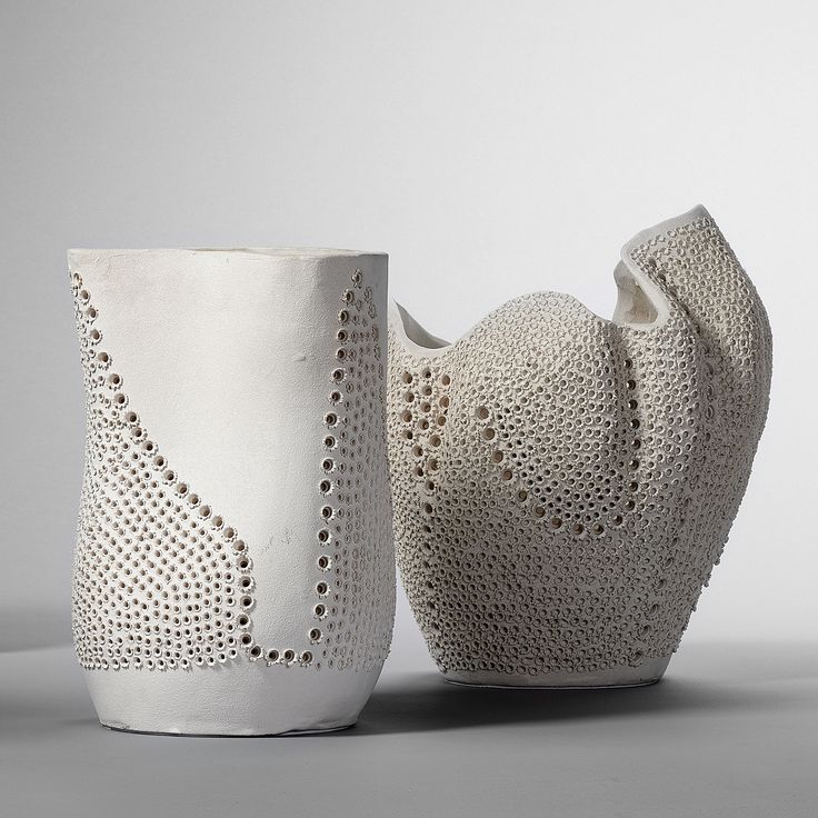 two white vases sitting next to each other on a gray surface with holes in them