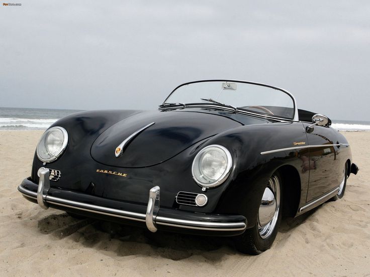 an old black sports car is parked on the sand at the beach in front of the ocean