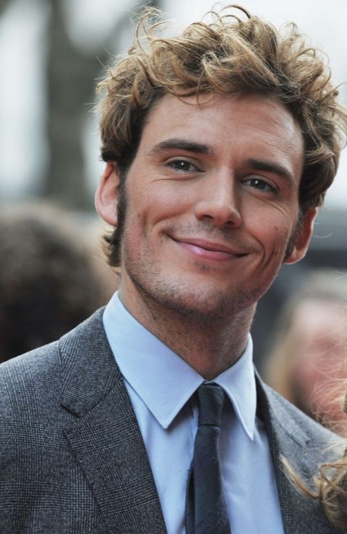 a man with curly hair wearing a suit and tie smiling at the camera while standing in front of a crowd