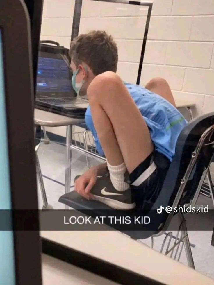 a young boy sitting in a chair with his feet on the desk while wearing a face mask