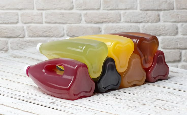 four different colored vases sitting on top of a wooden table next to a brick wall