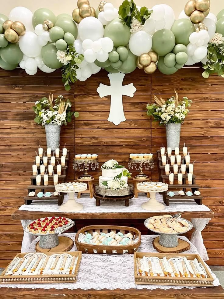 a table topped with lots of desserts next to a wall covered in balloons and greenery