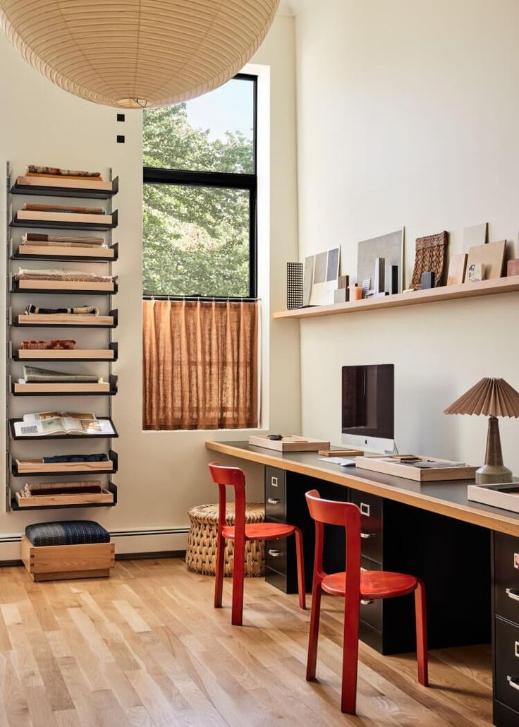 an office with two red chairs and a wooden desk in front of a large window