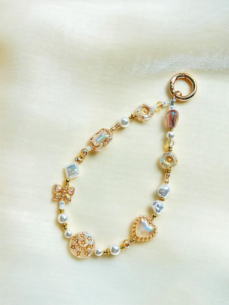 a close up of a bracelet on a white cloth with gold beads and charms in the shape of hearts