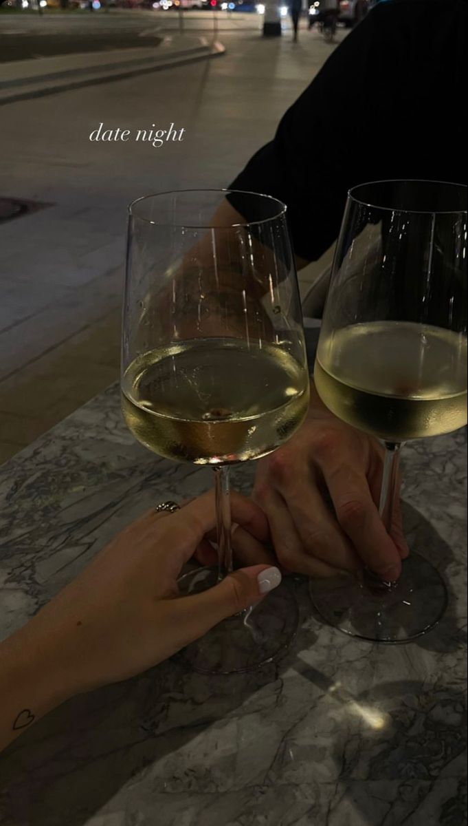 two glasses of white wine sitting on top of a marble table next to each other