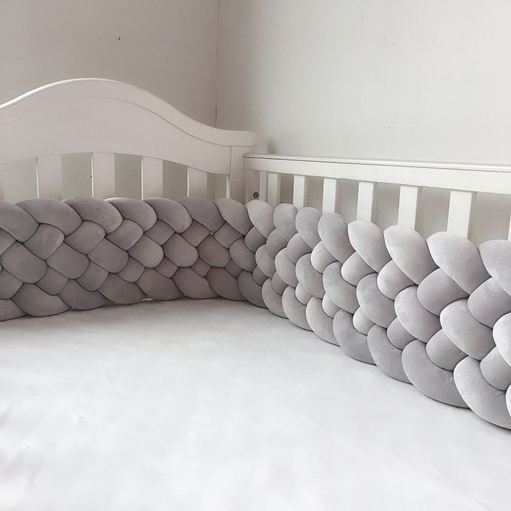 a crib bed with white sheets and gray pillows