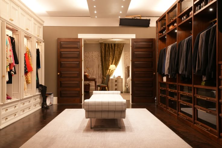 a large walk - in closet with lots of clothes on hangers and a footstool