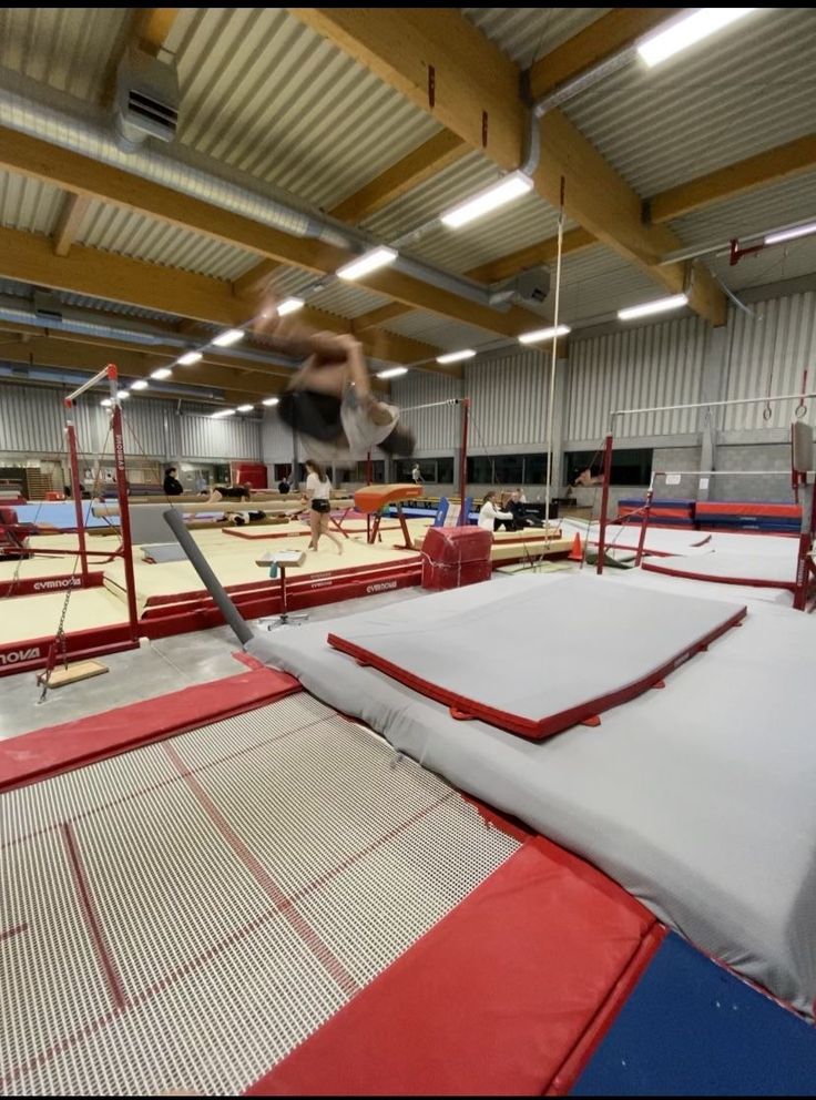 a man is jumping on a trampoline in an indoor gym with red and white mats