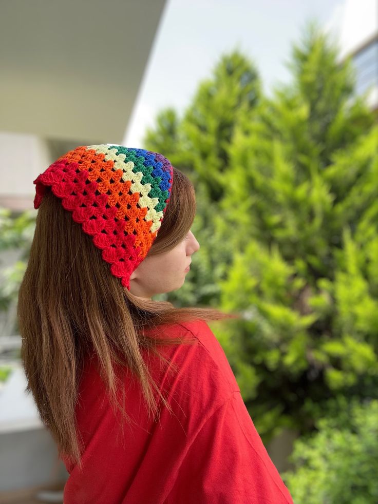 a woman wearing a colorful crochet headband in front of some trees and bushes