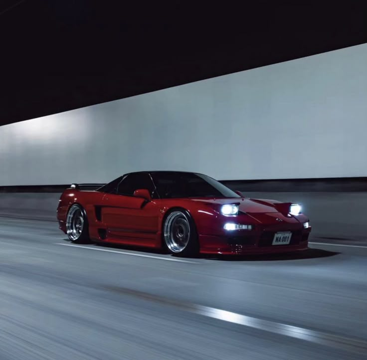 a red sports car driving down a street at night time with lights on it's headlamps