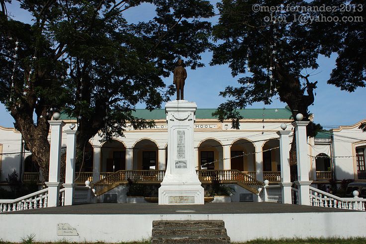 a statue in front of a white building with columns and arches on the sides, surrounded by trees