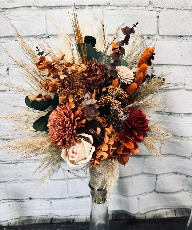 a vase filled with lots of different types of flowers next to a white brick wall