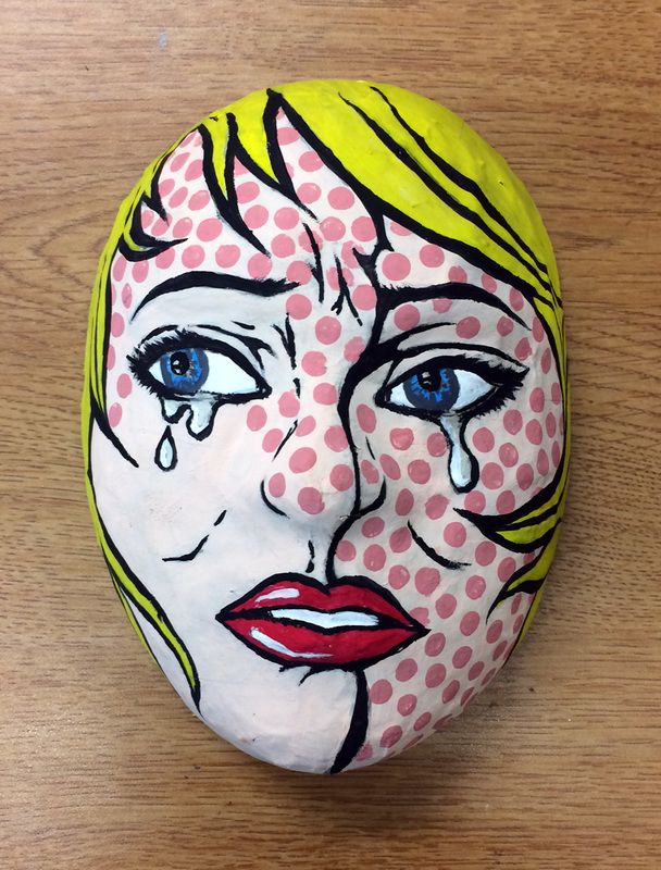 a painted rock with a woman's face and blue eyes on top of a wooden table