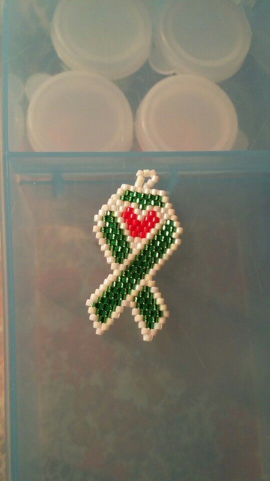 a beaded brooch with a green ribbon and red heart on it in a clear plastic container