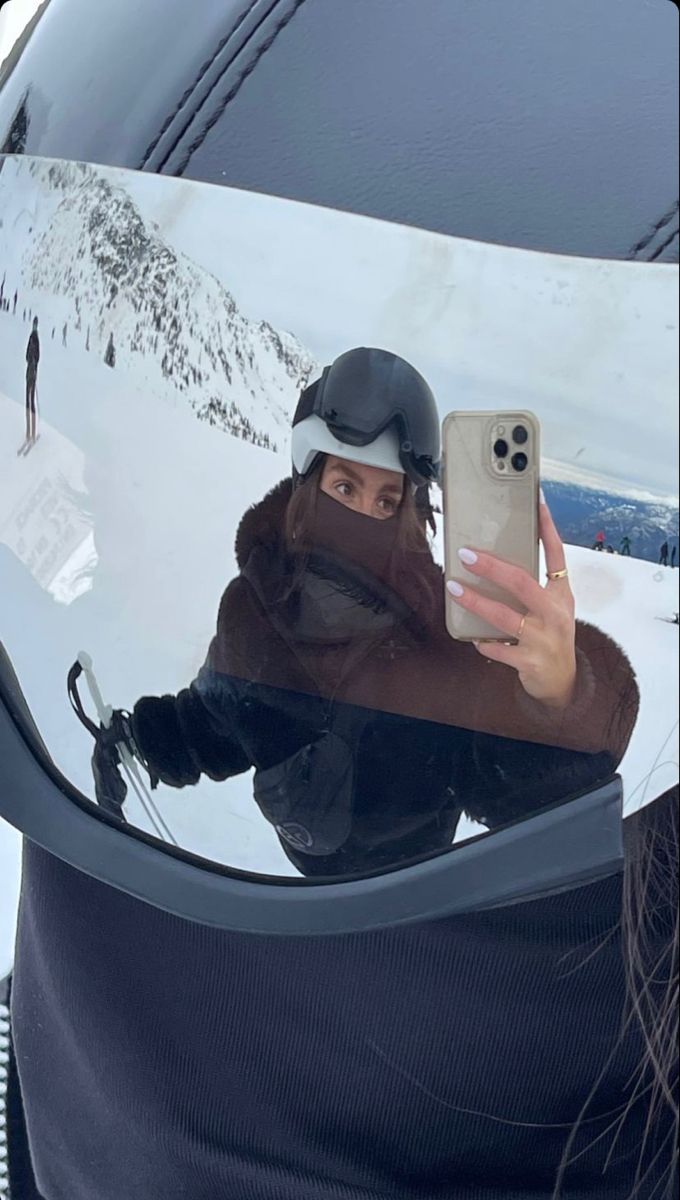 a woman taking a selfie in the mirror of a car with her ski gear on