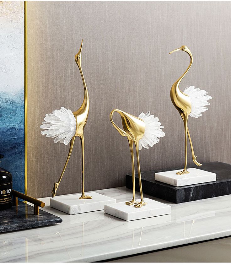 three gold flamingos are standing on marble bases