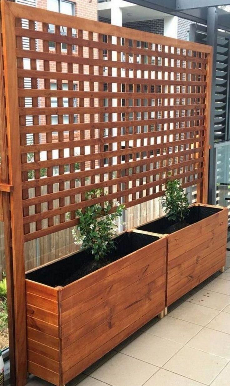 a wooden planter with two plants in it on the side of a building next to a fence