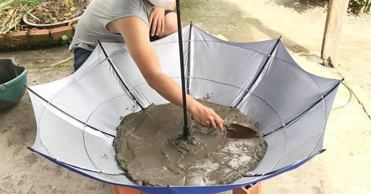 a woman in grey shirt holding an umbrella over a metal pan with dirt on it