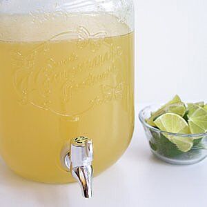 a glass jar filled with lemonade next to a bowl of limes