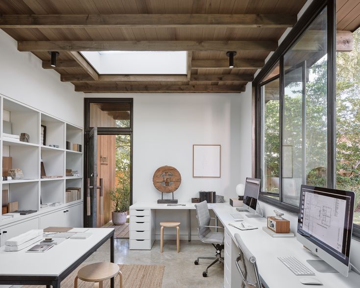 two people working in an office area with large windows and wooden ceilinging, along with white desks