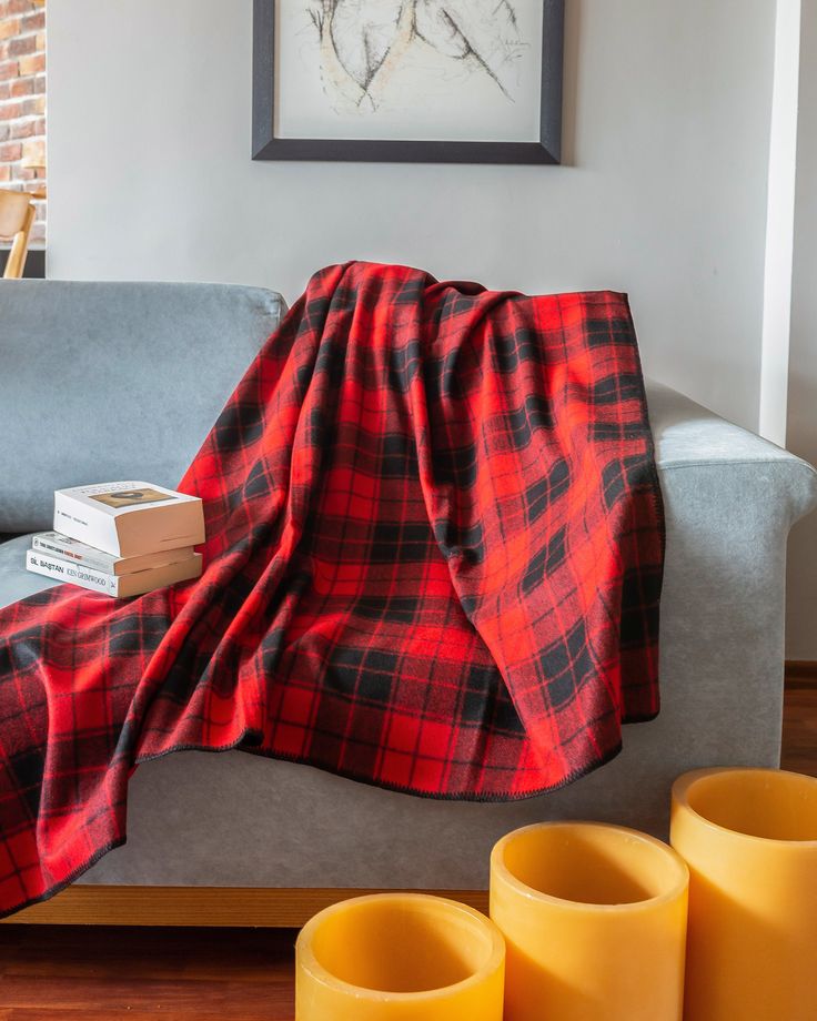 a red and black plaid blanket sitting on top of a couch next to two yellow vases