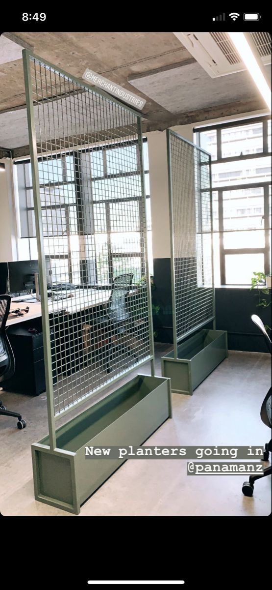 an office with two cubicles and desks in the middle, one has a metal screen divider