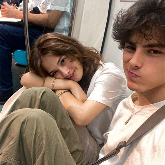 a young man and woman sitting next to each other on a subway train, looking at the camera