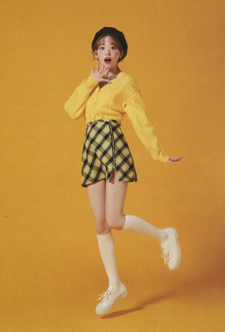 a woman in yellow sweater and plaid shorts posing for a photo with her hands on her face