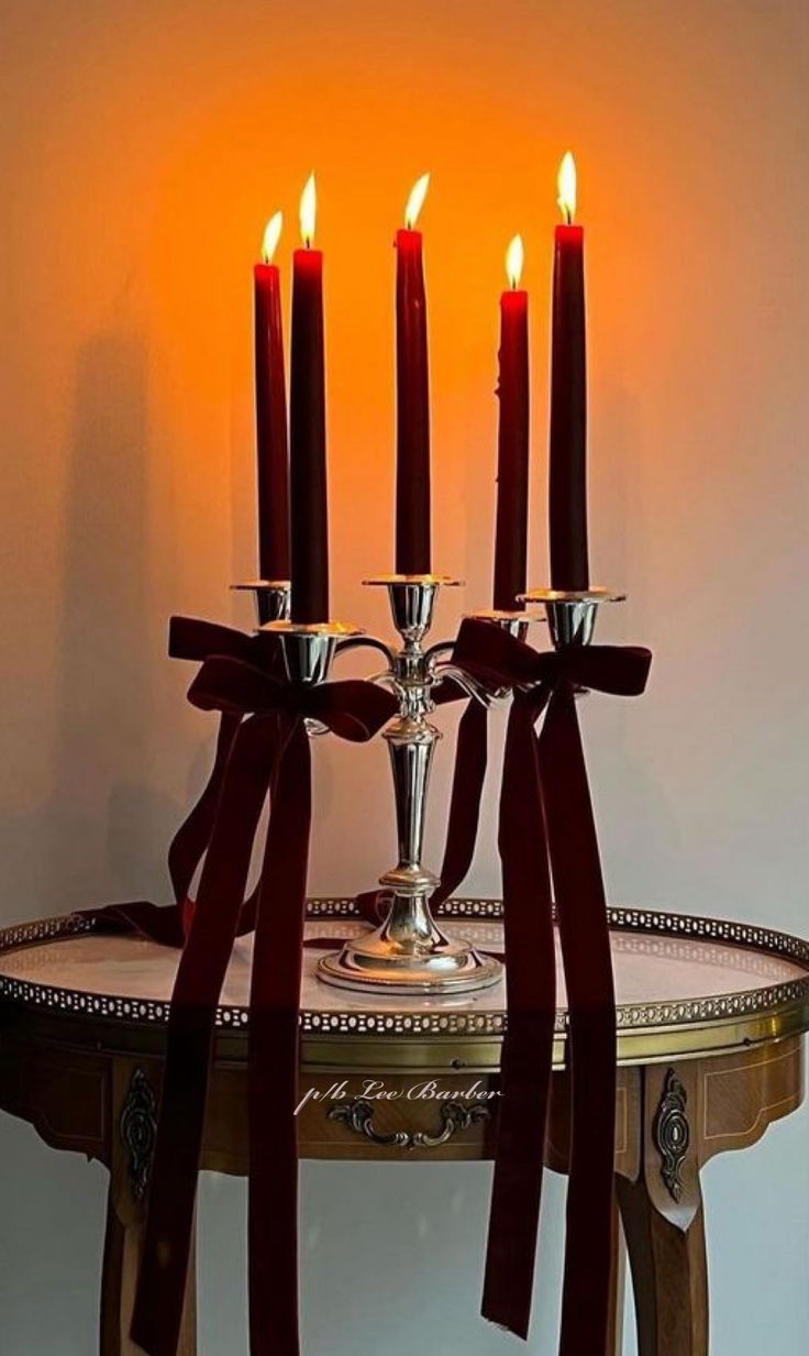 four candles are lit on a table with red ribbon around it and one candle is in the center