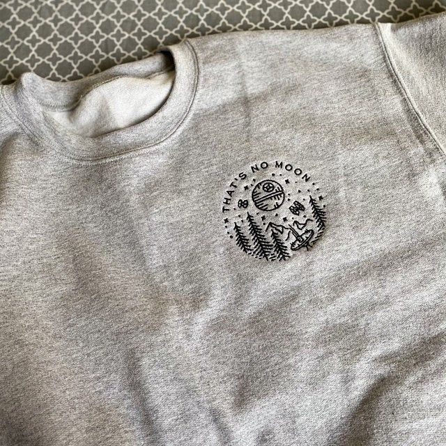 a grey sweatshirt with a black and white print on it sitting on a bed next to a pillow