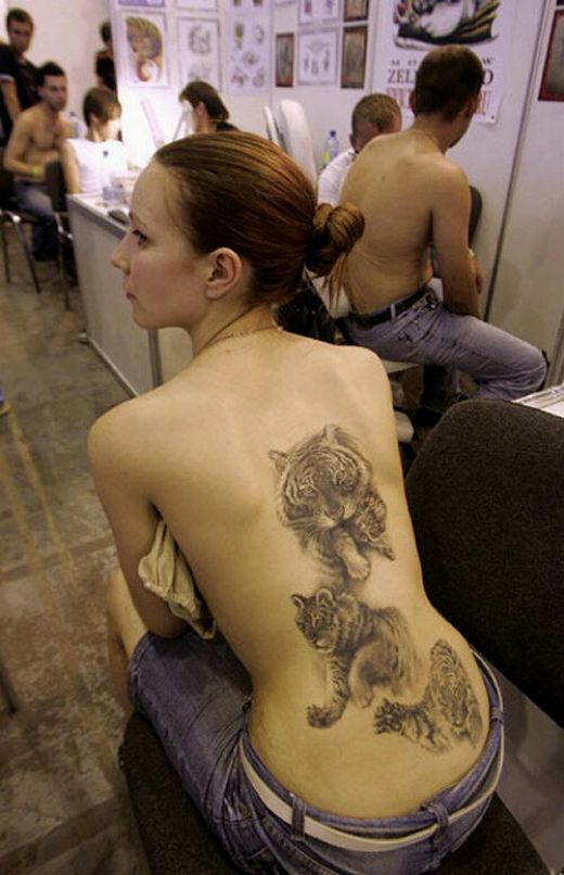 a woman with a tiger tattoo on her back sitting in an office cubicle next to other people