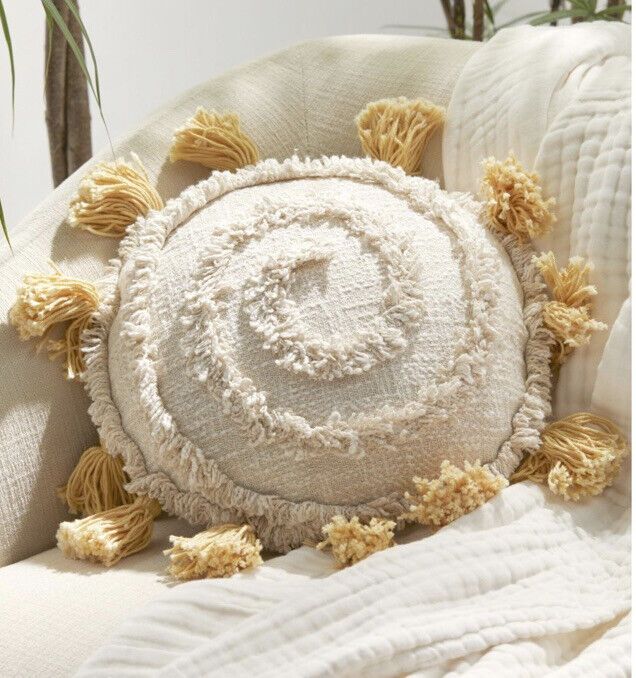 a white round pillow with yellow tassels on top of it sitting on a couch