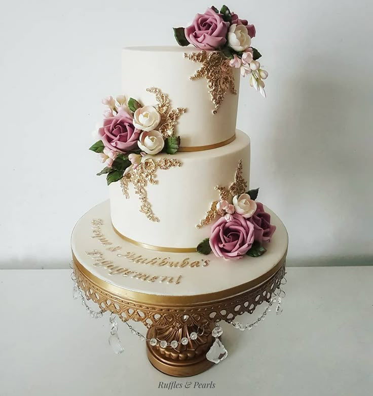 a three tiered wedding cake with pink and white flowers on the top, sitting on a gold stand