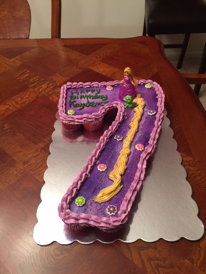 a purple and yellow birthday cake with the number seven on it sitting on a table