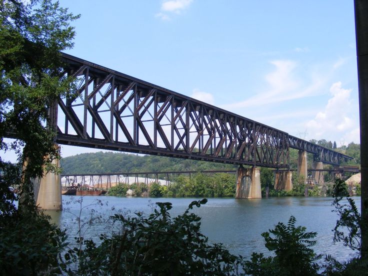 an old train bridge over a large body of water with trees in the foreground