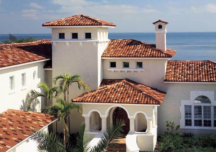 an aerial view of a house with red tile roofing and white walls, overlooking the ocean