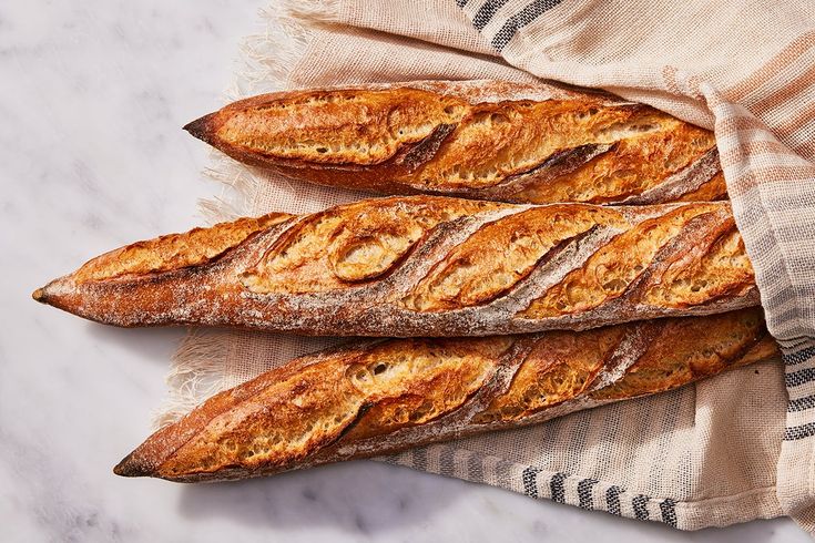 three loaves of bread sitting on top of a towel next to a baguette