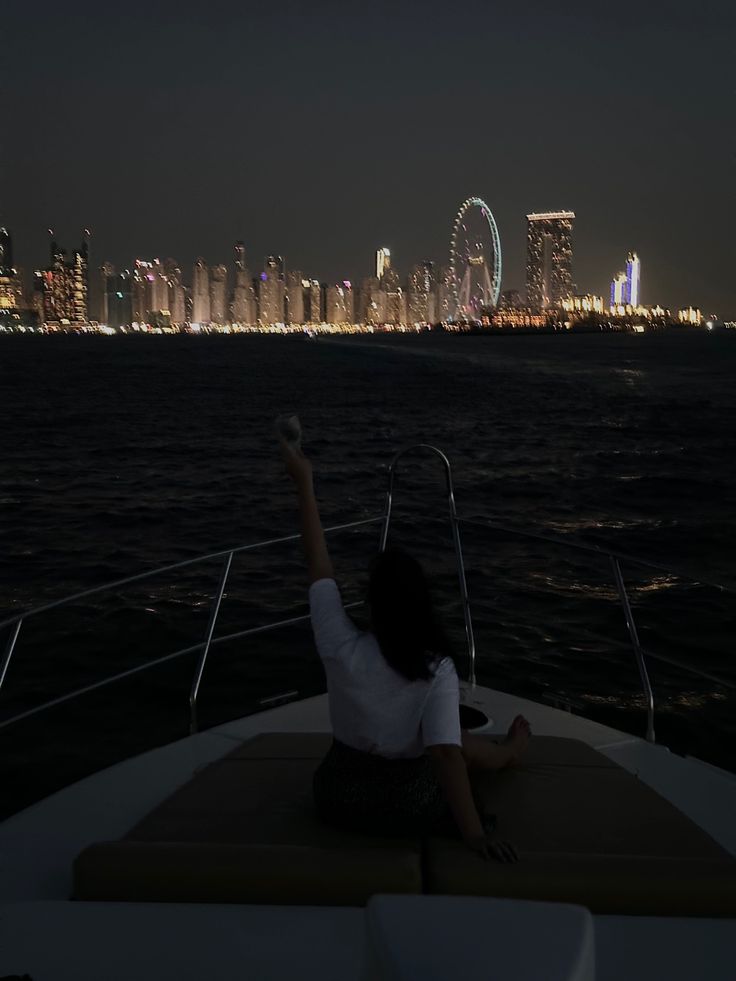 a woman sitting on the back of a boat at night with her arm in the air