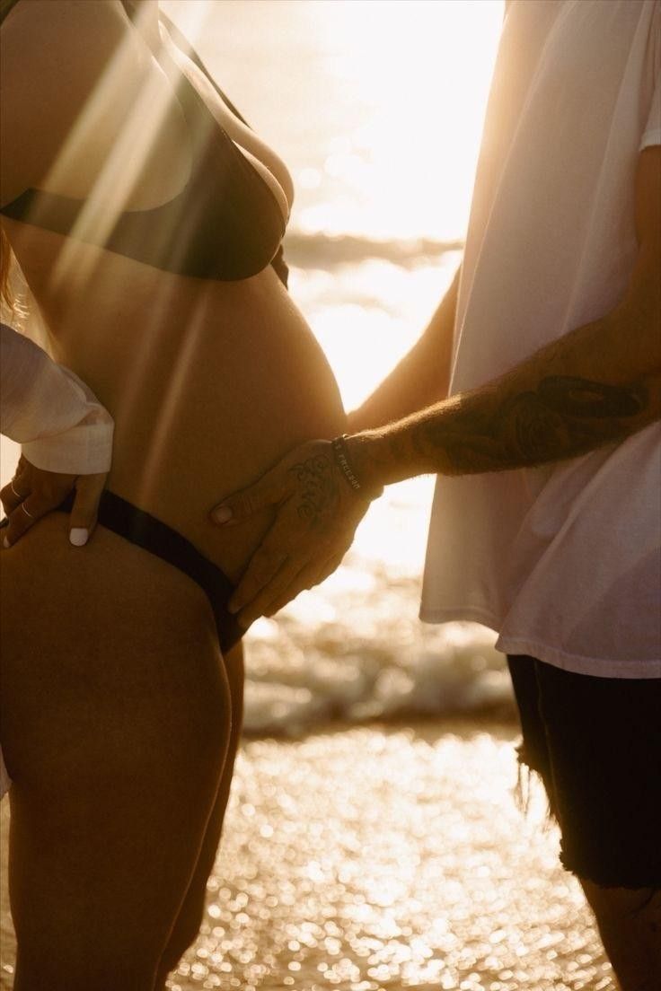 a man and woman standing next to each other in front of the ocean at sunset