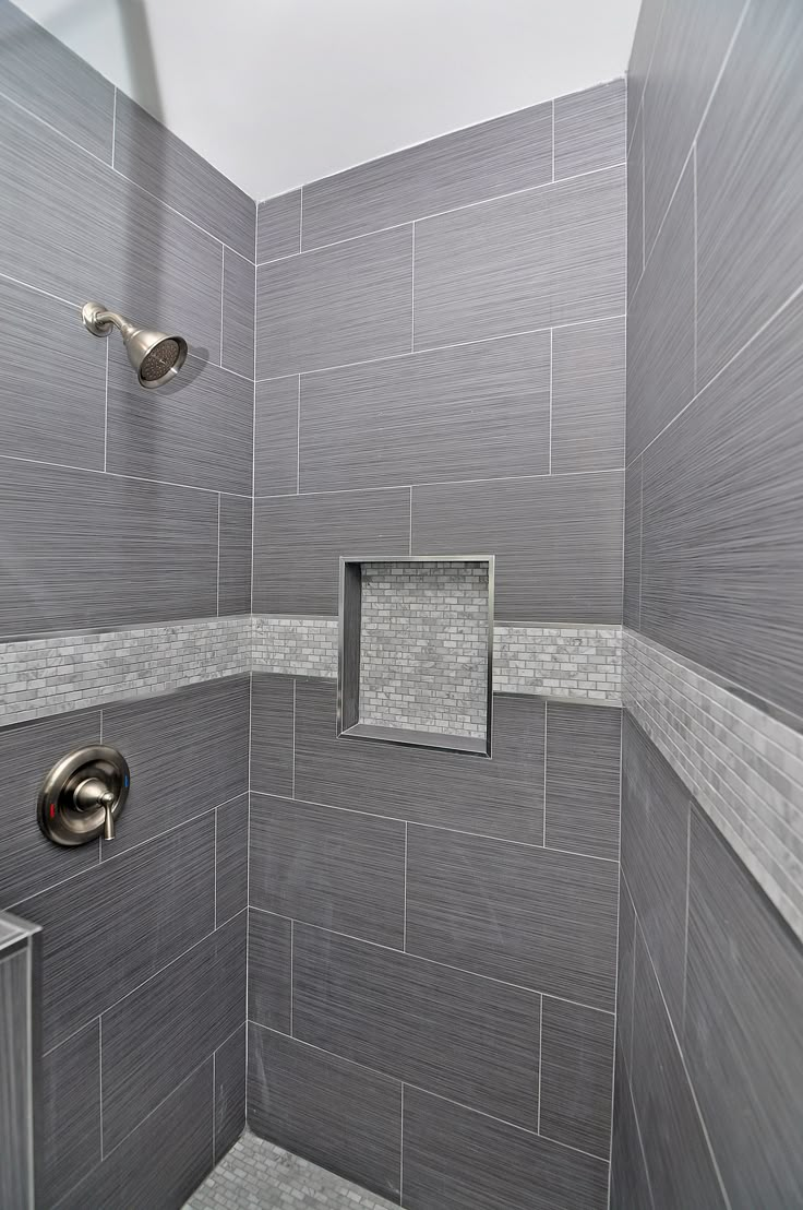 a walk in shower sitting next to a tiled wall and floor covered in gray tiles