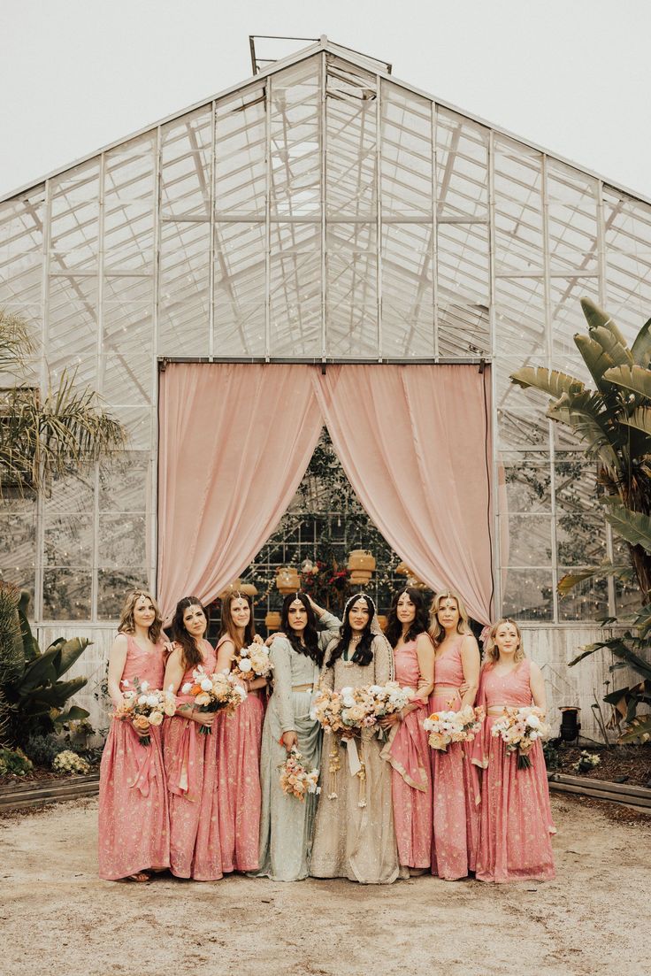 a group of women standing next to each other in front of a building with pink drapes