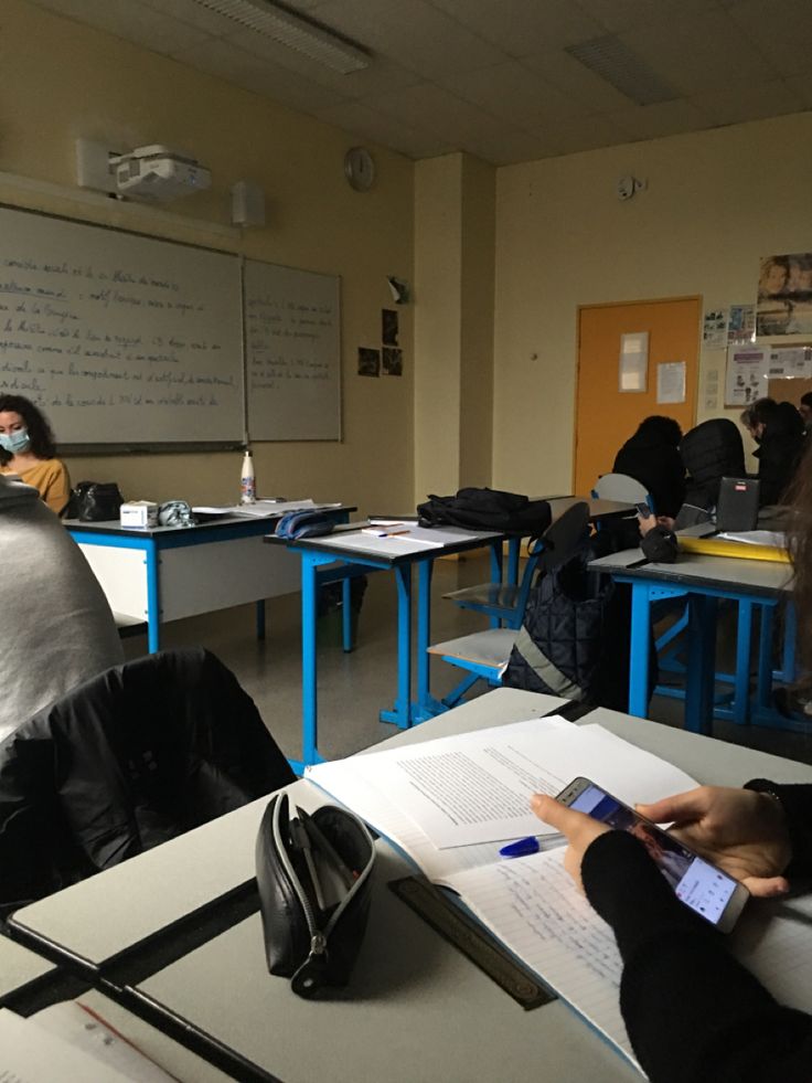 several people sitting at desks in a classroom with books and papers on the desk