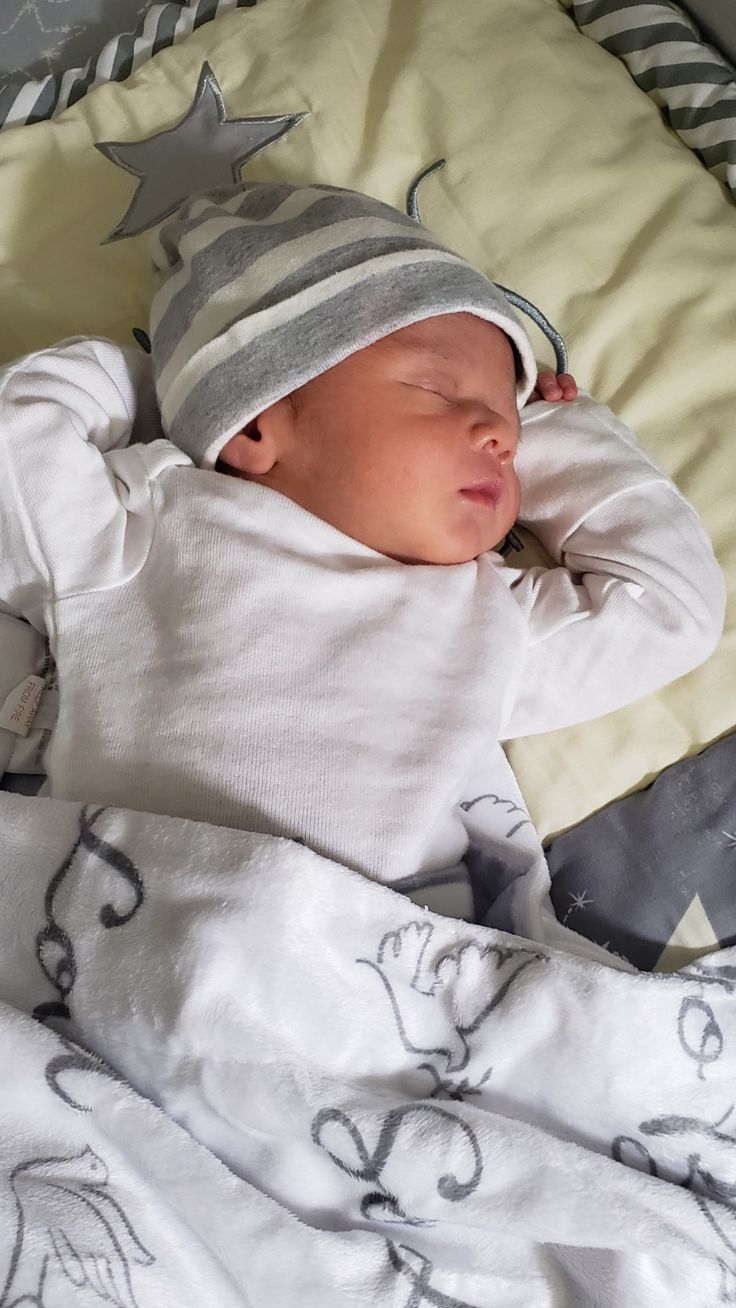 a baby sleeping on top of a bed wearing a hat and blanket with stars around it