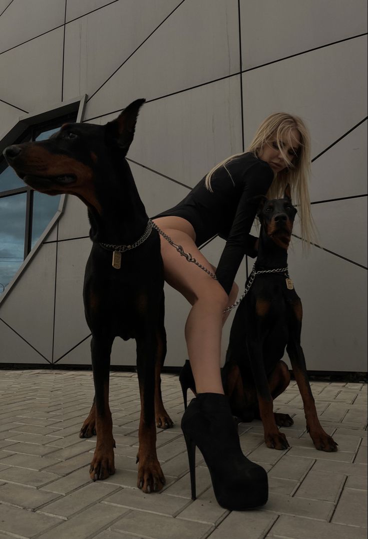 a woman is posing with two dogs in front of a large building and wearing high heeled boots