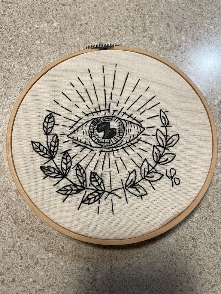 an embroidered eye with leaves around it on a counter top next to a pair of scissors