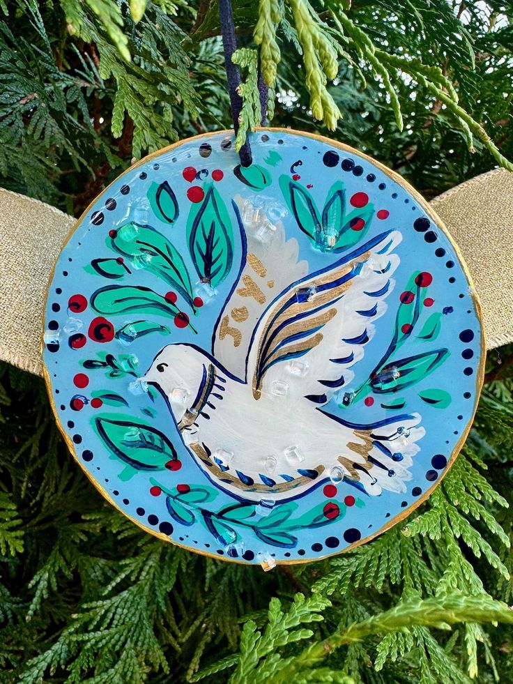 an ornament hanging from a christmas tree decorated with blue and gold designs, featuring a dove